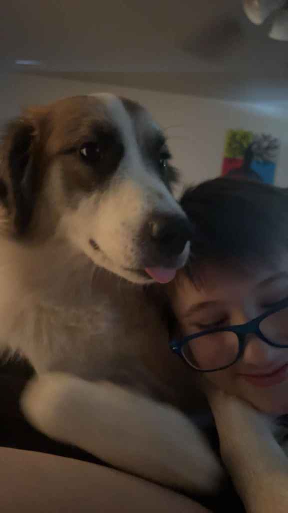 Picture of Braydin wearing glasses cuddling his dog who's sticking out her tongue. 
